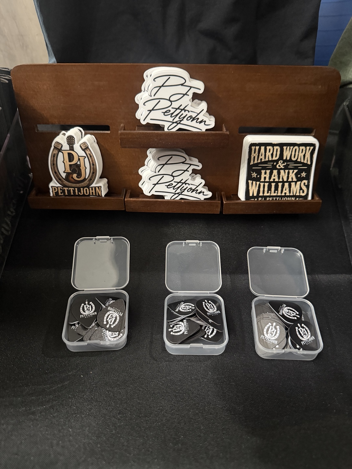 PJ Pettijohn signature, horseshoe, and Hard Work and Hank Williams stickers above three boxes of branded guitar picks